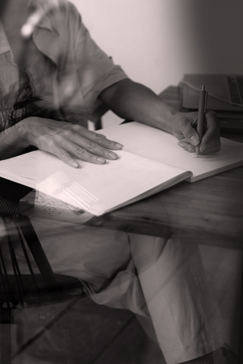 Person sitting at a desk and writing by hand on a notepad.